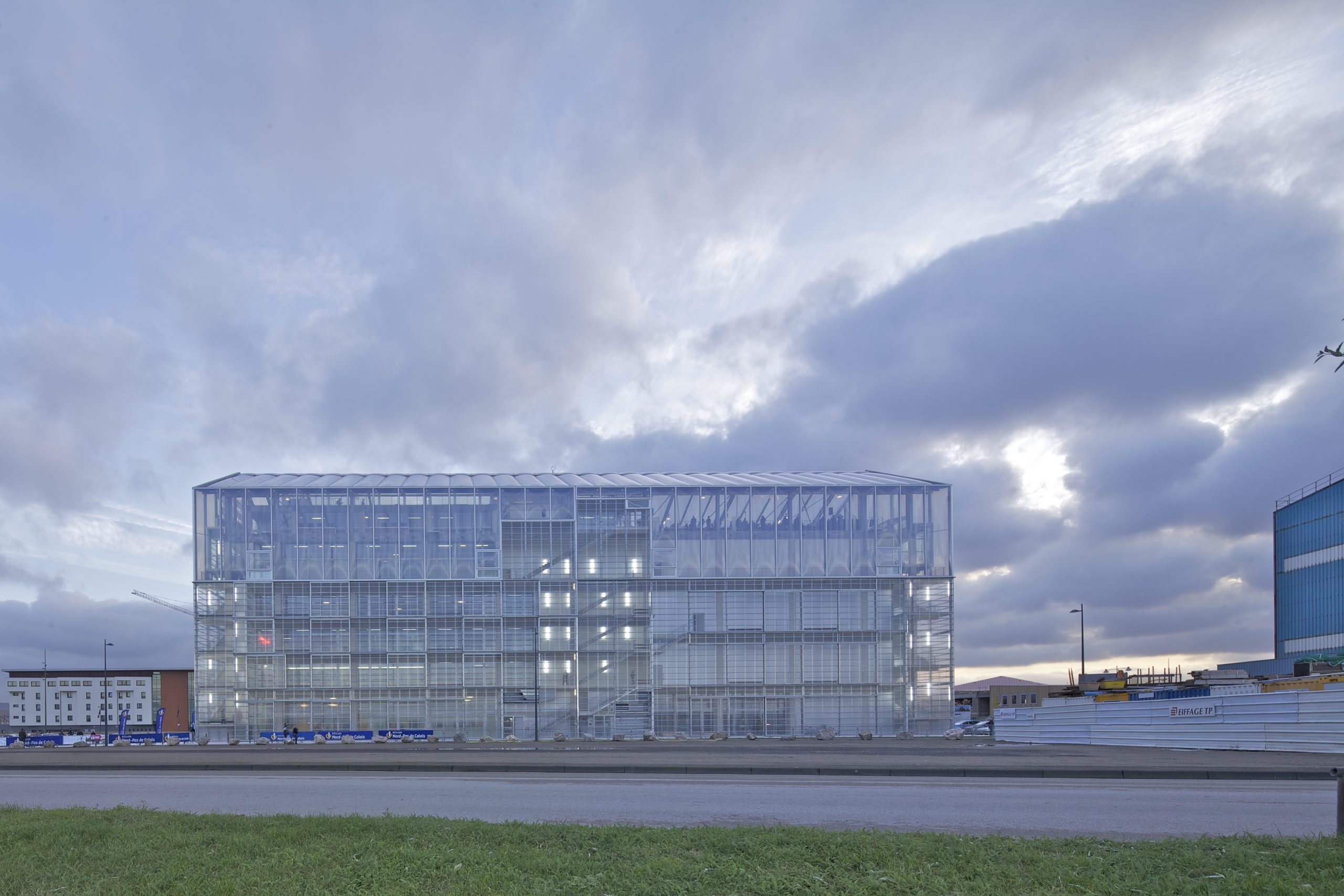 Ein modernes Glasgebäude mit transparenter Gitterfassade steht am Flughafen unter bewölktem Himmel.