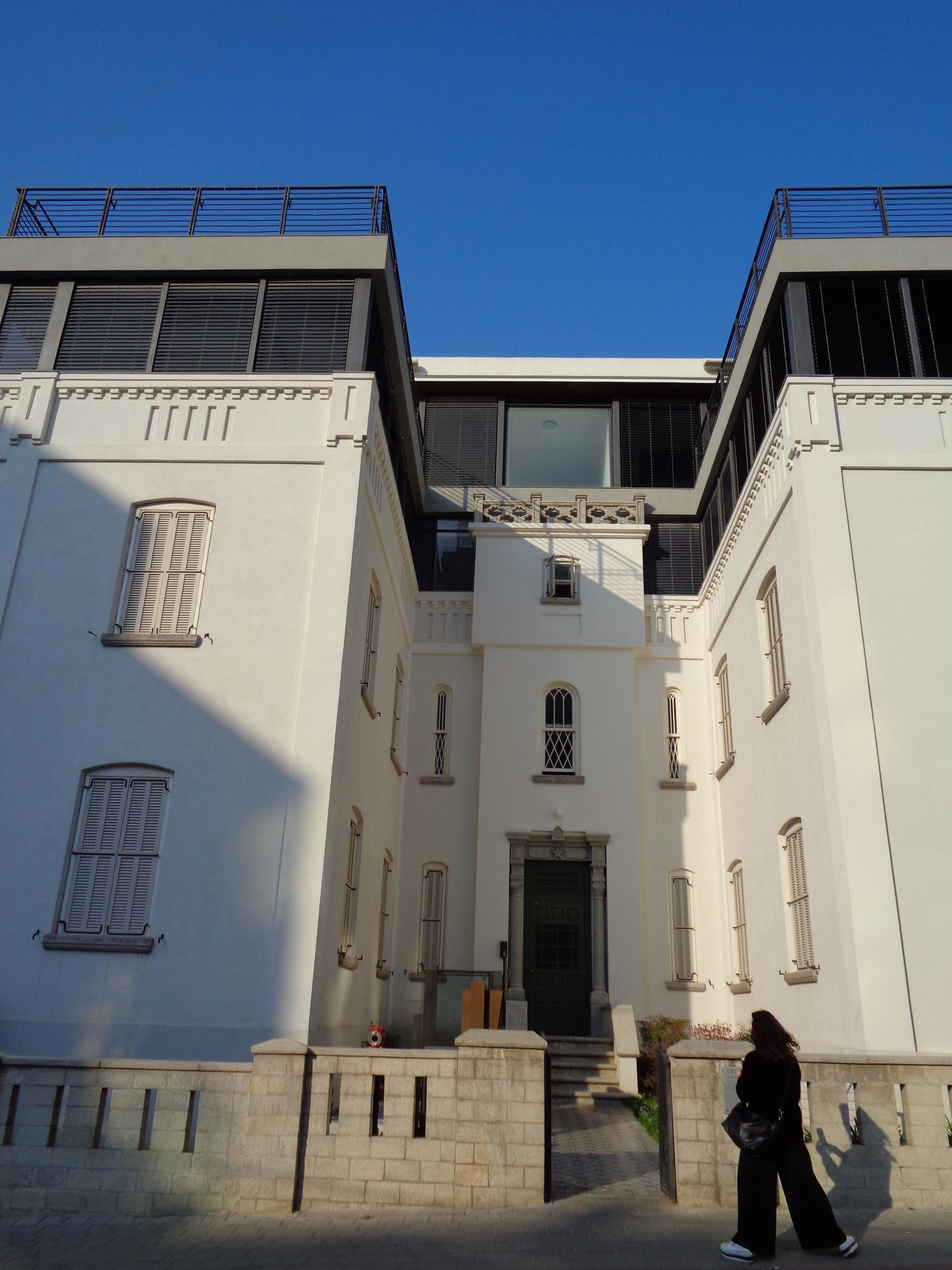 Ein modernes Gebäude mit weißer Fassade kombiniert klassische Architekturelemente mit zeitgenössischen Flachdächern und Glasflächen unter blauem Himmel.