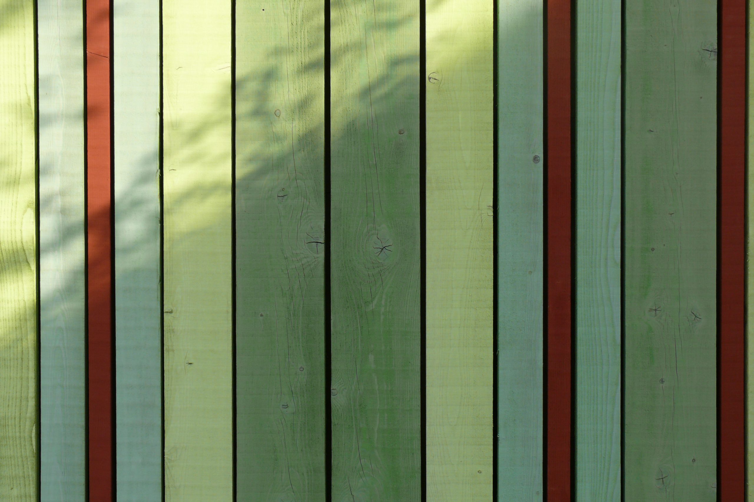Vertikale Holzlamellen in Creme, Grün und Rostrot bilden eine moderne Fassade mit Schattenspiel.