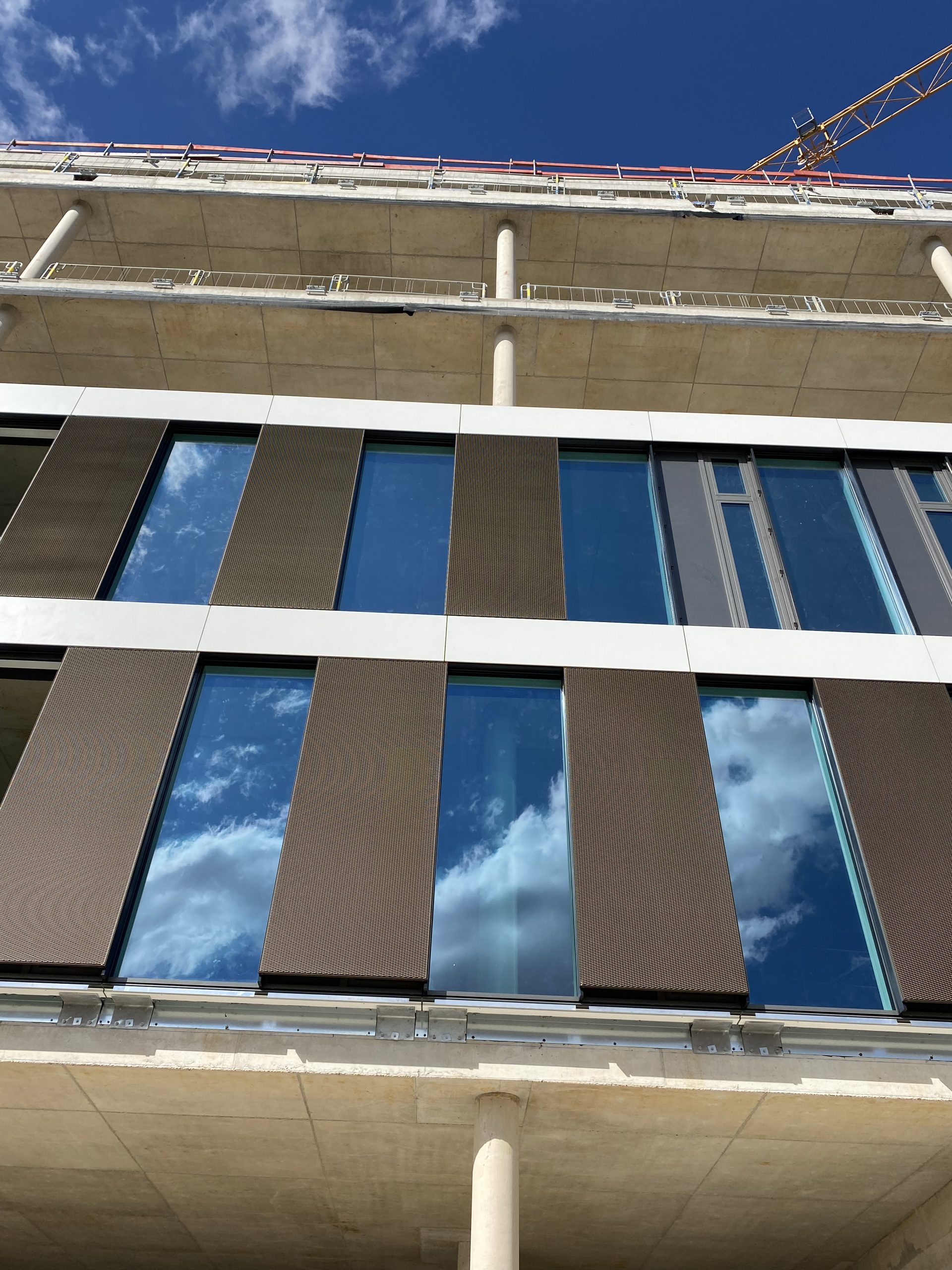 Ein modernes Hochhaus mit wechselnder Fassade aus braunen Metallpaneelen und großen Glasfenstern, die den Himmel spiegeln.