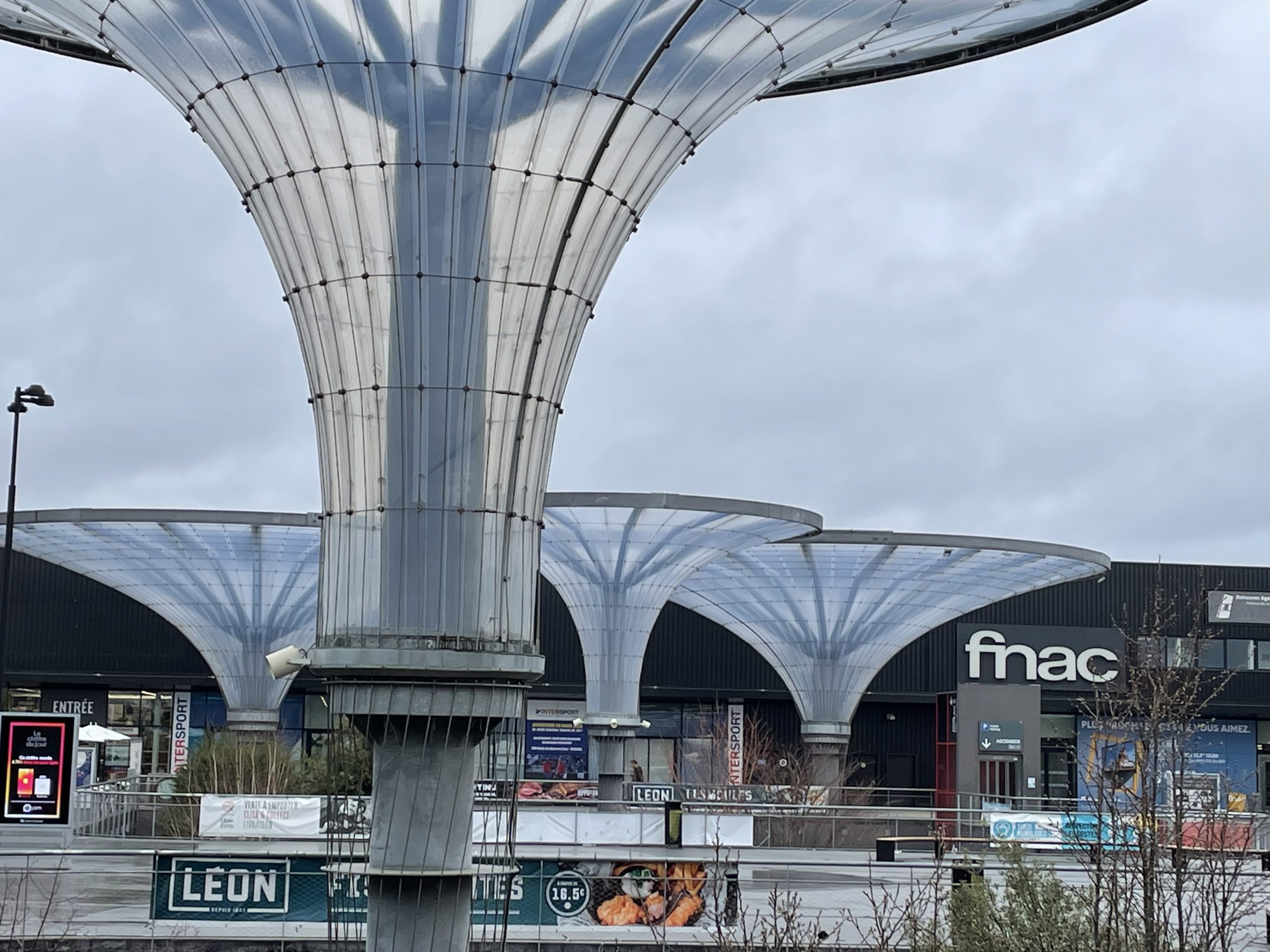 Eine beeindruckende moderne Architektur mit geschwungenen Glasdächern über einem Einkaufszentrum mit dunkler Metallfassade.