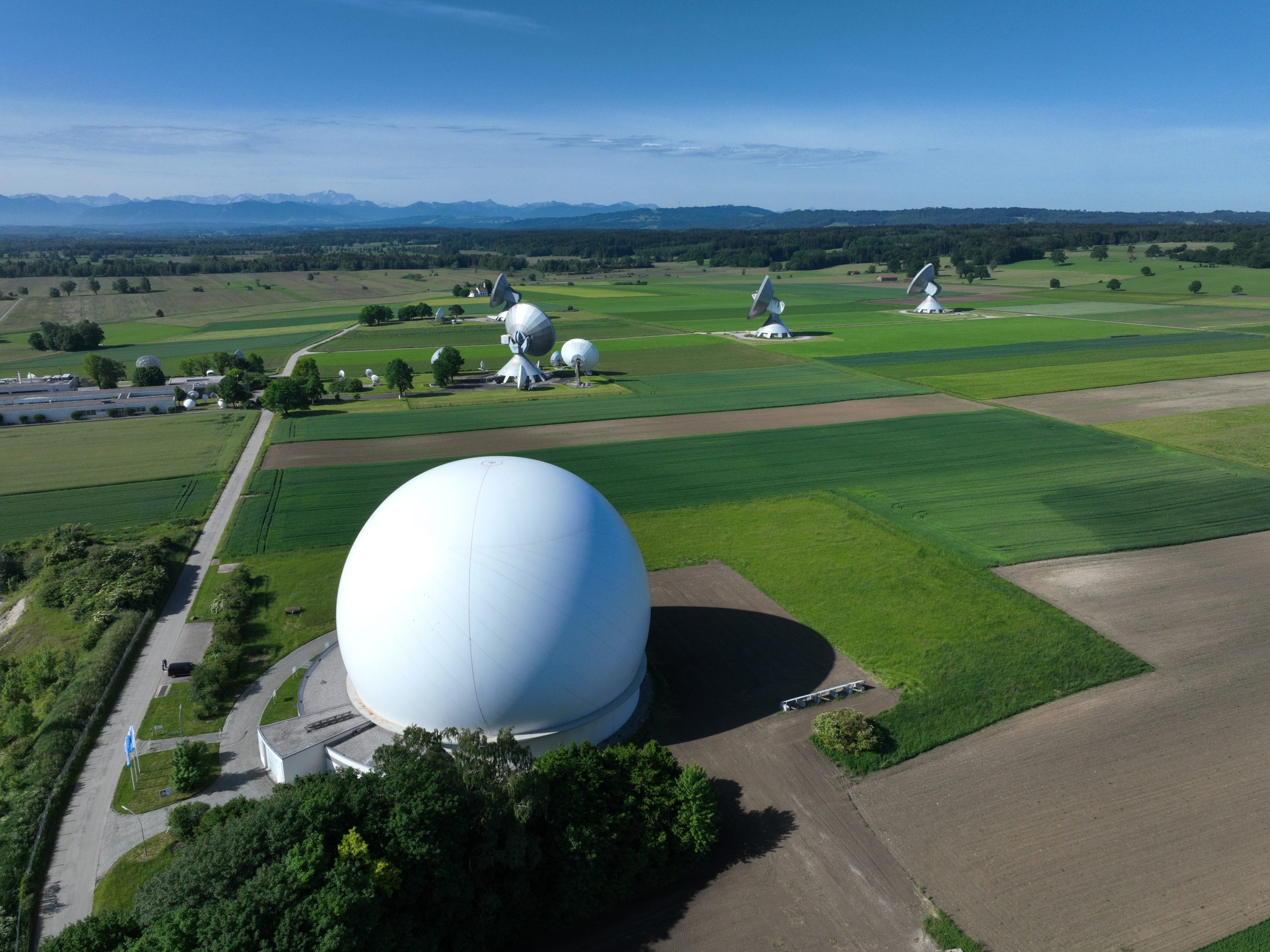 Eine massive weiße Kugel mit geschwungener Architektur sitzt inmitten grüner Felder und Wiesen in einer ländlichen Landschaft.