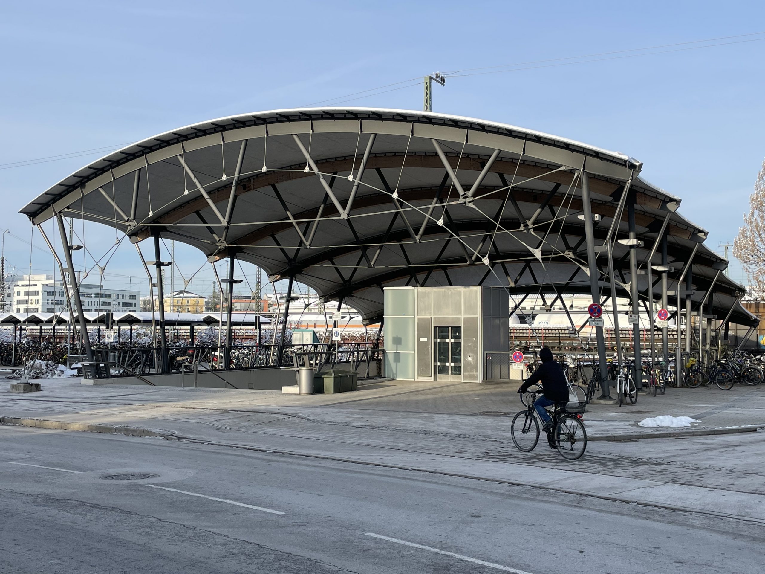 Ein modernes Fahrradparkhaus mit geschwungener Metallkonstruktion und zentralem Servicegebäude in minimalistischem Design.