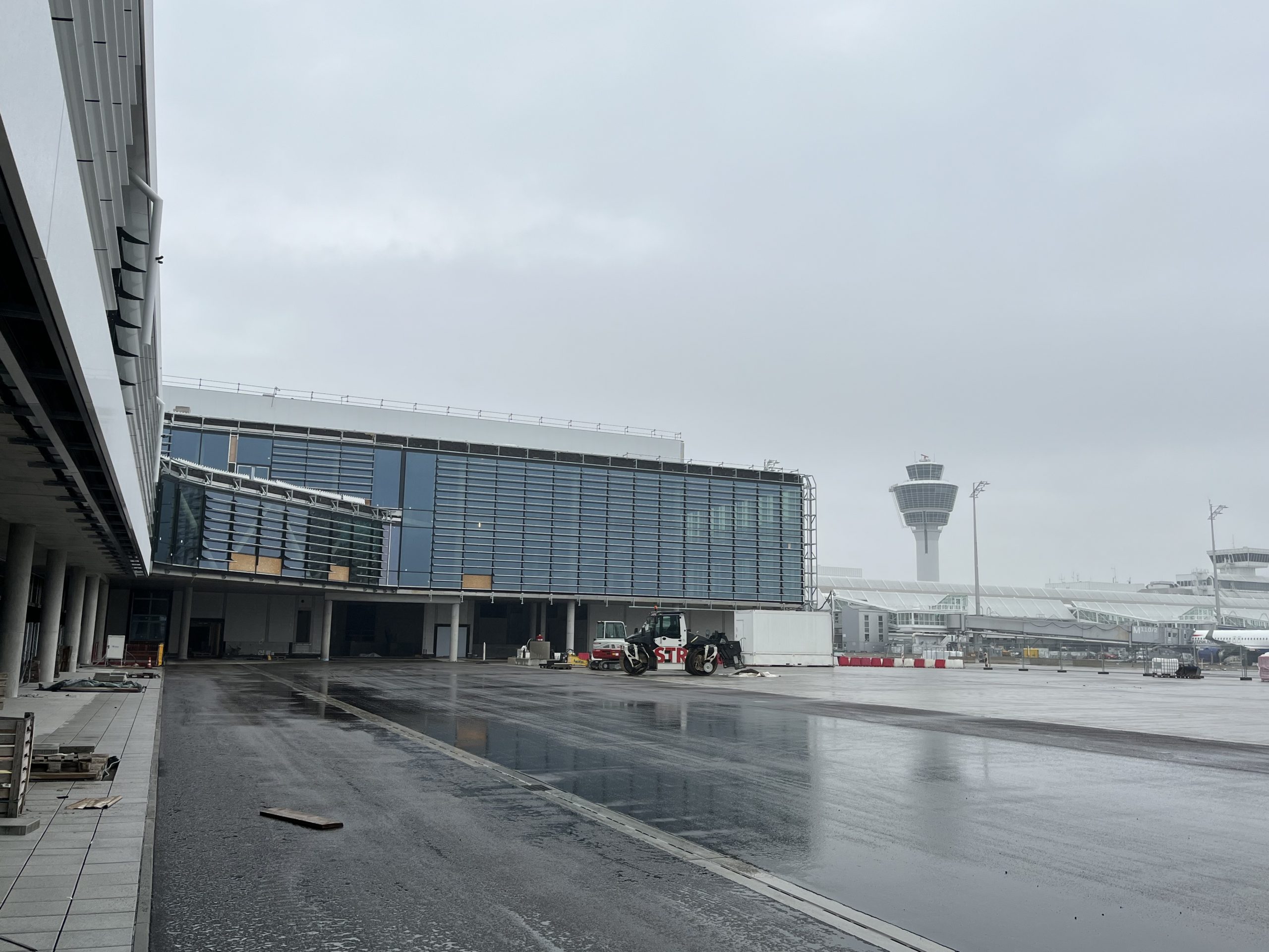 Ein modernes Flughafengebäude mit Glaskonstruktion und Metallrahmen steht neben einem Kontrolltower unter bedecktem Himmel.