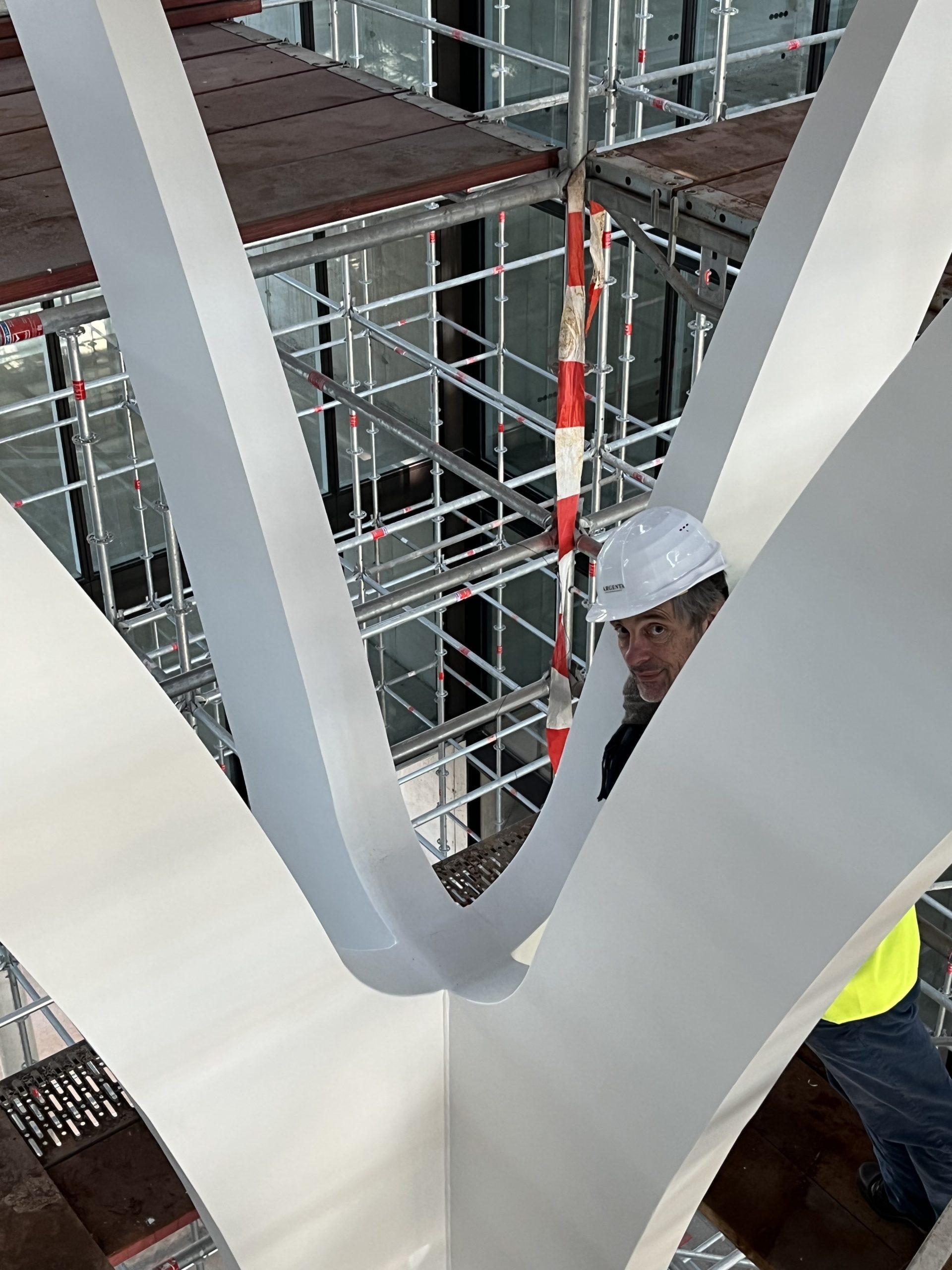 Ein Arbeiter in Schutzausrüstung steht in einem modernen Treppenschacht mit Metallgerüst und weißen Betonwänden.