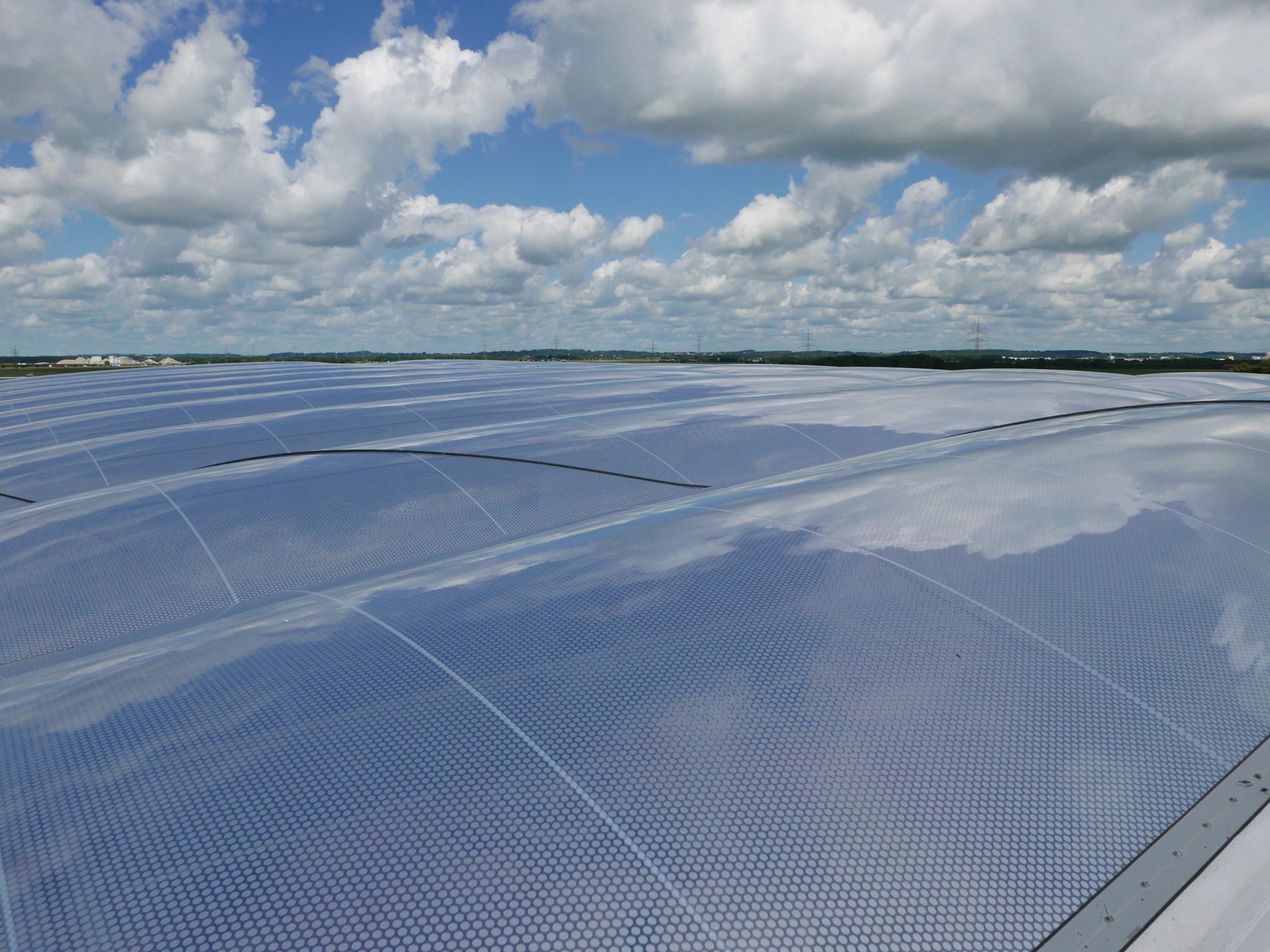 Eine ausgedehnte Solaranlage mit blauem Modulraster erstreckt sich unter bewölktem Himmel über die flache Landschaft.