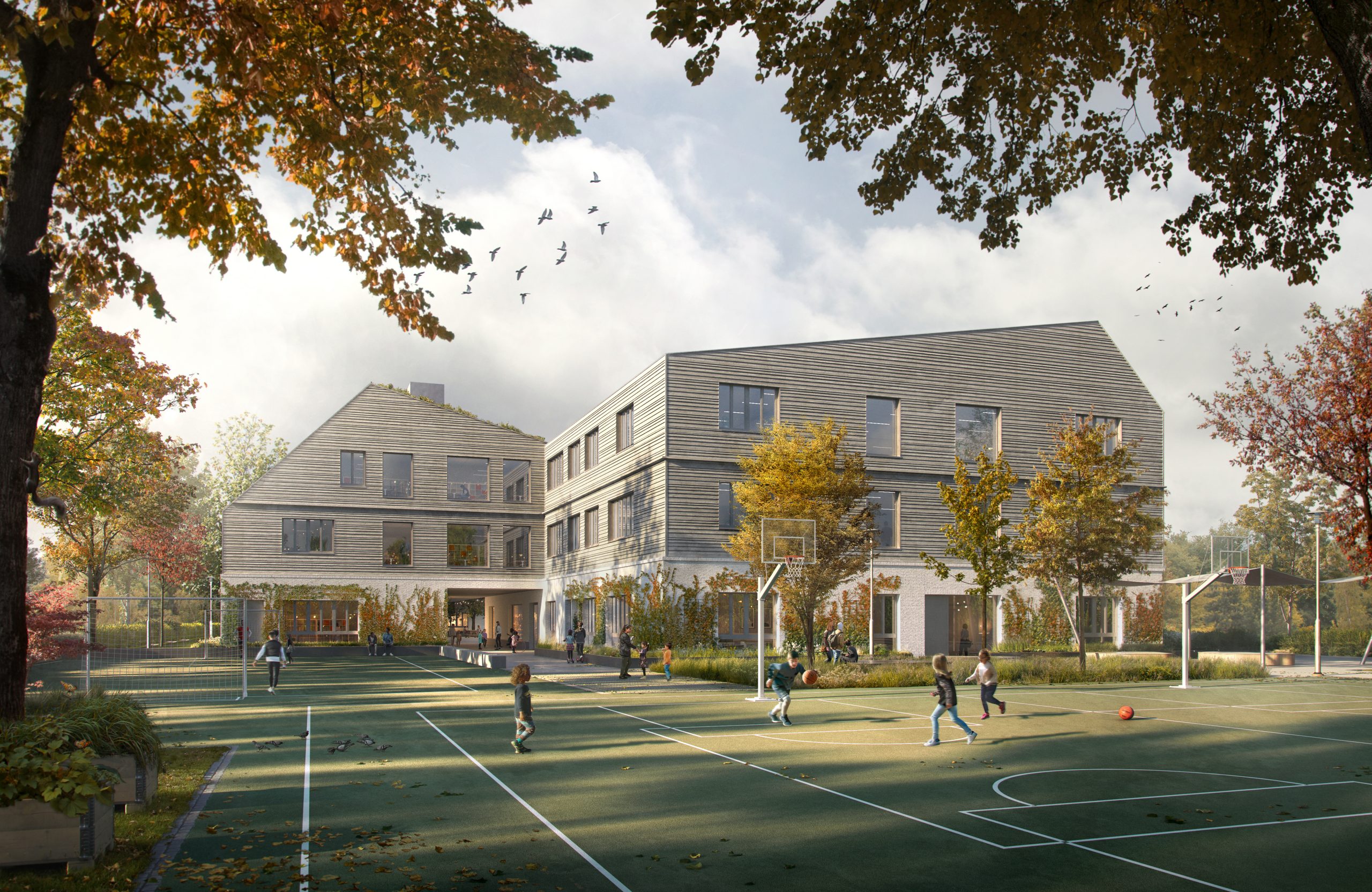 Ein modernes Schulgebäude mit grauer Metallverkleidung und Satteldächern liegt in herbstlicher Parklandschaft mit Sportplatz.