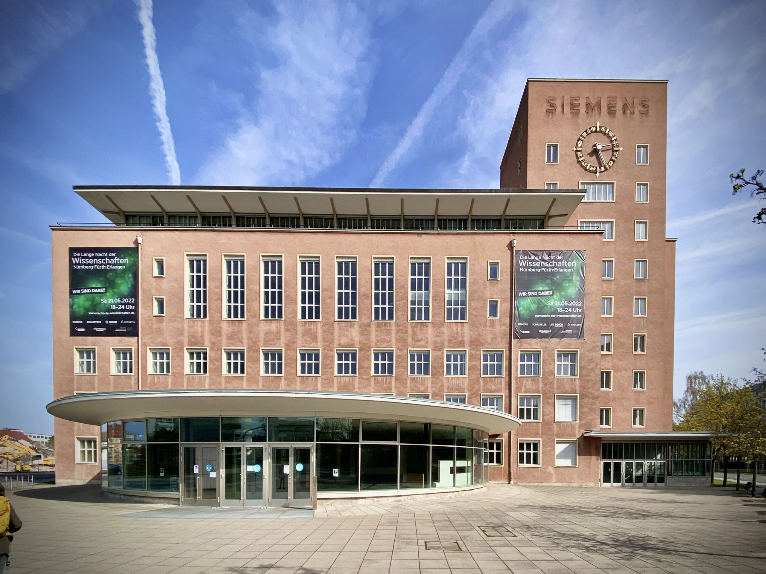 Das Siemens-Gebäude zeigt moderne Backsteinarchitektur mit geschwungenen Fassadenelementen, großflächigen Fenstern und einer charakteristischen Uhr.