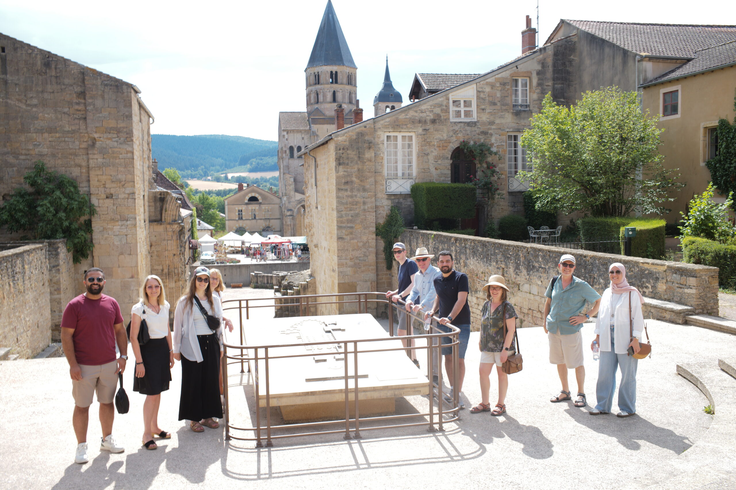 Besuchergruppe von FTR und LEF-T auf einem historischen Platz des ursprünglichen Hauptschiffes mit Steinbauten und Kirchturm im Hintergrund.